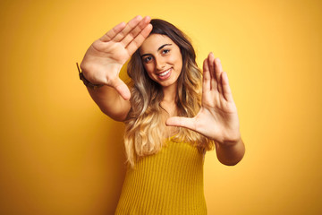 Poster - Young beautiful woman wearing t-shirt over yellow isolated background doing frame using hands palms and fingers, camera perspective