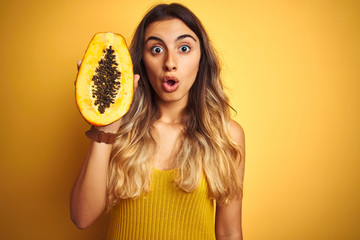 Sticker - Young beautiful woman holding papaya over yellow isolated background scared in shock with a surprise face, afraid and excited with fear expression