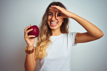 Canvas Print - Young beautiful woman eating red apple over grey isolated background with happy face smiling doing ok sign with hand on eye looking through fingers