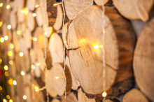 Background Of Natural Wooden Saw Cuts And Christmas Garland. Christmas Background Made Of Wood And Lights For Text Close-up And Copy Space.