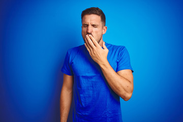 Wall Mural - Young handsome man wearing casual t-shirt over blue isolated background bored yawning tired covering mouth with hand. Restless and sleepiness.