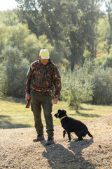 Wall Mural - Hunting period, autumn season open. A hunter with a gun in his hands in hunting clothes in the autumn forest in search of a trophy. A man stands with weapons and hunting dogs tracking down the game.	