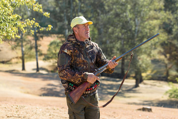 Wall Mural - Hunting period, autumn season open. A hunter with a gun in his hands in hunting clothes in the autumn forest in search of a trophy. A man stands with weapons and hunting dogs tracking down the game.	