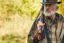 Senior Caucasian Man With Hunting Gun Looking Away, Man With Grey Beard Wearing Hunting Clothes Outdoors. Forest Background