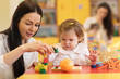 © Oksana Kuzmina - Children with teachers playing with color wooden puzzle in a montessori classroom