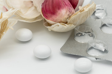 Close-up of mock-up Garlic Supplements seen outside their packaging. Seen next to an opened Garlic bulb, showing some isolated Garlic cloves. The image depicts how Garlic supplements are refined.