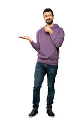 Full-length shot of Handsome man with sweatshirt holding copyspace imaginary on the palm to insert an ad over isolated white background