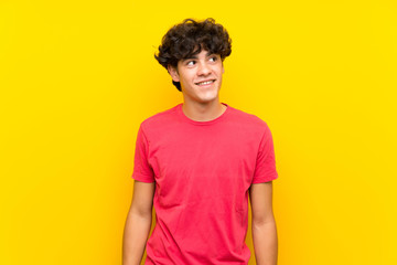 Young man over isolated yellow wall laughing and looking up