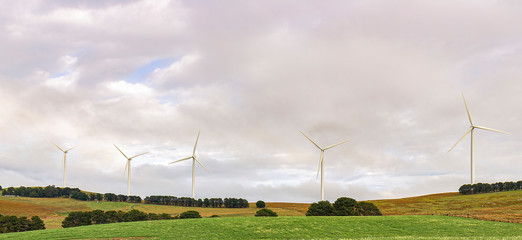 Wall Mural - an array of large wind turbines moving to create kinetic energy for renewable energy supply on a clo