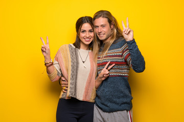 Hippie couple over yellow background smiling and showing victory sign with both hands