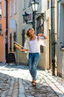© ako-photography - A beautiful woman in a light hat, with long blond hair, a white blouse and blue jeaans in the middle of old town street - image