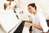 Lady in white shirt play the piano indoors at home.