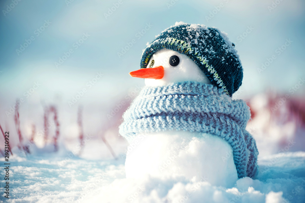 Little cute snowman in a knitted hat and scarf on snow on a sunny ...