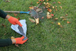 The gardener holds a granular fertilizer in his hands next to a fan rake and autumn leaves against a lawn background.