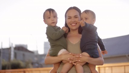 medium portrait shot with lens flare of happy asian mother standing outdoors on sunny day, holding h