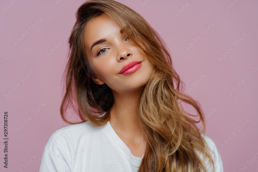 Portrait of satisfied relaxed young female model tilts head, has makeup, fair hair, dressed in white clothes, poses against purple background, has well cared complexion. People, beauty, face care - obrazy, fototapety, plakaty 