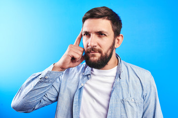 Wall Mural - Clever bearded man shows finger on the smart head, brain and mind, encourages you to think well isolated in blue studio