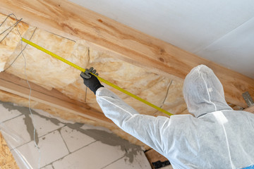 Wall Mural - Professional builder man installing thermal insulation layer with fiberglass wool under the roof