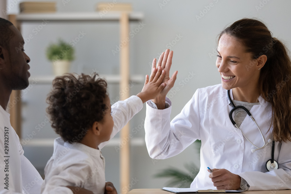 Smiling female doctor give high five to little biracial patient - obrazy, fototapety, plakaty 