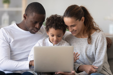 Wall Mural - Smiling international family with kid using laptop at home