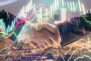 Double exposure of financial graph on cityscape background with two businessman handshake. Concept of stock market deal