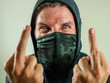 © TheVisualsYouNeed - young man as fanatic and aggressive anarchist rioter giving middle finger. furious and scary violent anti-system protester in face mask screaming hostile at fighting riot