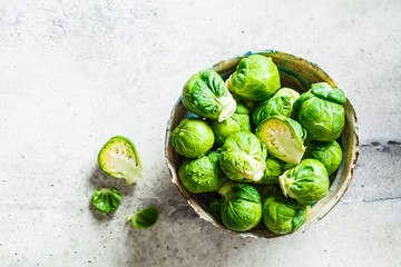 Raw brussels sprouts in bowl, gray concrete background, top view. Healthy vegan food concept.