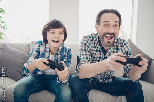 Portrait of two nice attractive cheerful cheery glad guys dad and pre-teen son spending day playing online video game at light white modern style interior house living-room indoors