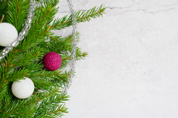 fragment of a christmas tree or fir branches decorated with christmas decorations toys balls, on the background of a white concrete wall. 