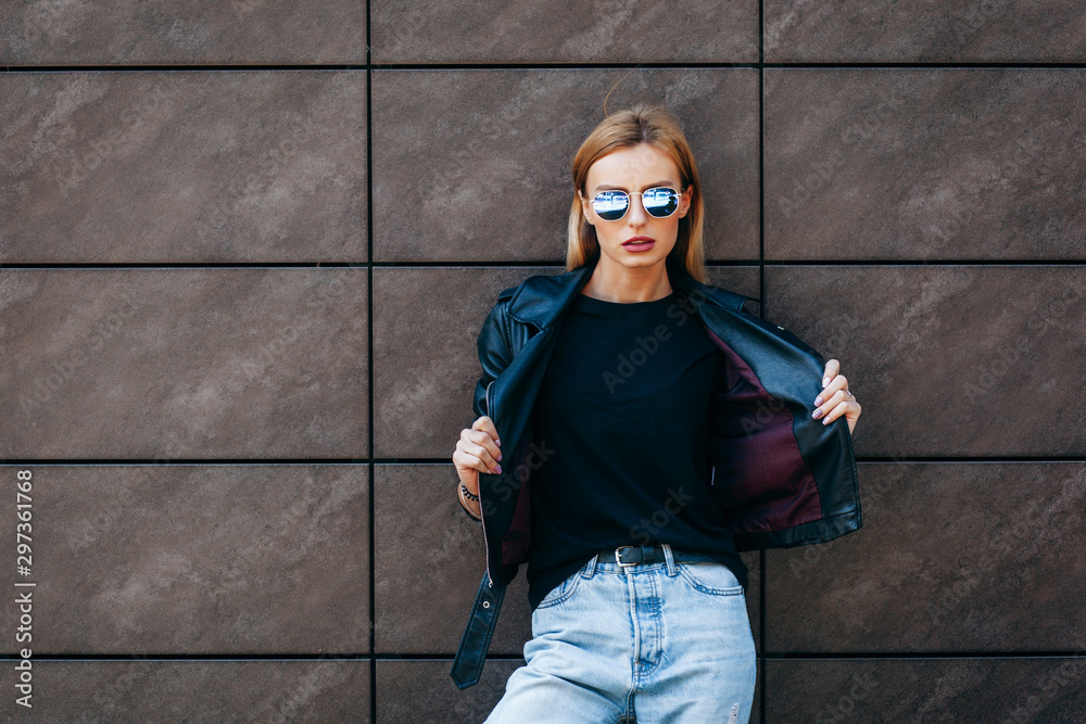 Girl wearing t-shirt, glasses and leather jacket posing against street , urban clothing style. Street photography