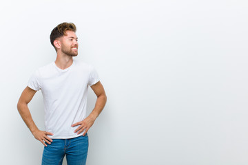 young man looking happy, cheerful and confident, smiling proudly and looking to side with both hands on hips against white background