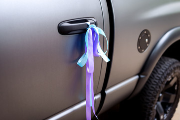 Colorful ribbons on a grey car, decoration for wedding transport. Closeup.