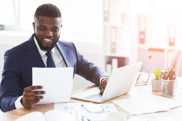 Satisfied black businessman checking documents, sitting in modern office