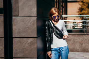 Wall Mural - Stylish model girl at the city in black leather jacket and white sweater and glasses with waist bag
