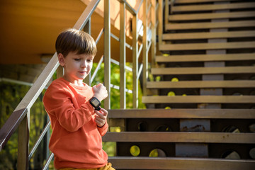 Photo of the boy looking at a smart watch. Children and modern technology. Kid calling to his friends or parents after school