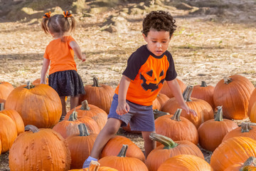 a small boy walks over the pumpkins in the opposite direction of the little girl. visiting at the lo