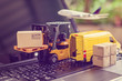 © William W. Potter - Logistics, supply chain and delivery service concept : Fork-lift truck moves a pallet with box carton. Van on a laptop computer, depicts wide spread of products around globe in ecommerce popular era