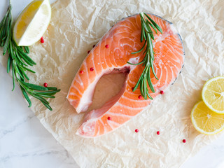 Delicious salmon steak with lemon slices, spices and rosemary , rich in omega 3 oil, on light table. Healthy and diet food. Fresh uncooked red fish. Cooking salmon, seafood. Top view