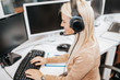 Beautiful blond smiling female call-center agent with headset working on support in the office.