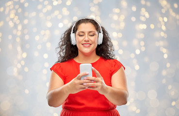 Wall Mural - people, electronics and technology concept - happy woman in wireless headphones listening to music on smartphone over festive lights background