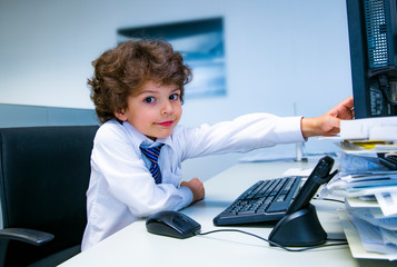 Cute beautiful little boy children play as office worker sitting on working desk using business computer and touching monitor.