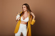 Beautiful busty young woman with long hair in white lingerie and yellow jacket keeping a small dog, and posing at the orange background, isolated. Sexy girl with a perfect body posing with chihuahua