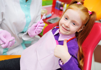 children's dentist examines the teeth and mouth of the child - a cute red-haired girl sitting in a dental chair. Pediatric dentistry