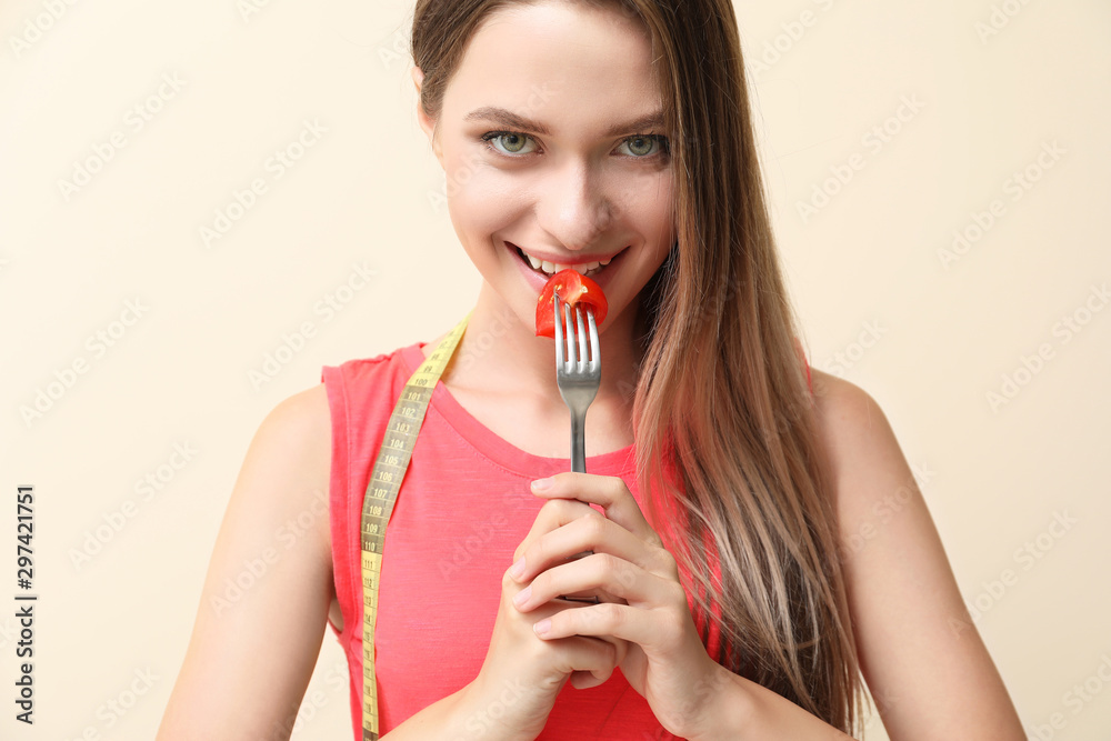 Woman with fresh tomato on fork and measuring tape on light background. Diet concept