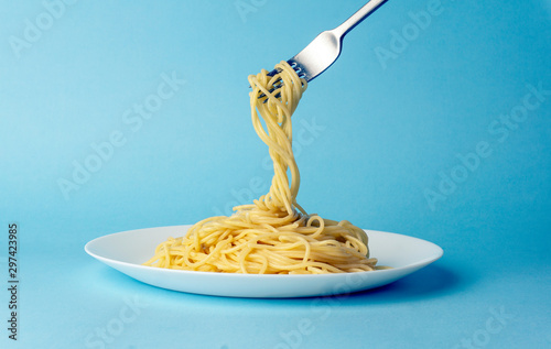 Fotografía Spaghetti pasta with a fork on a white plate on a blue background