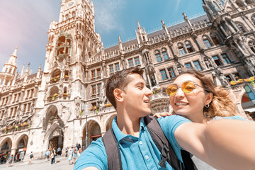 Wall Mural - happy multinational couple in love hugs and takes a selfie photo on the background of The city hall tower in Munich. Honeymoon trip to Germany