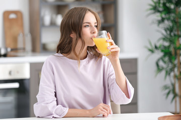 Beautiful young woman drinking orange juice in kitchen