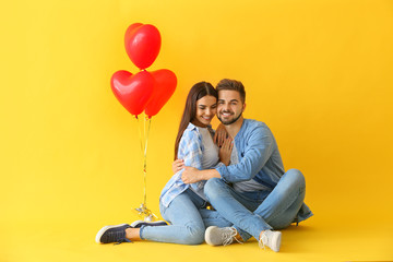 Portrait of beautiful young couple with air balloons on color background