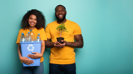 Wall Mural - Happy couple hold a plastic container and a small tree over a light blue color. Concept of forestation, ecology, conservation, recycling and sustainability