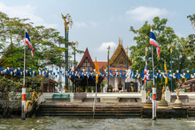 Bangkok City, Thailand - March 17, 2019: Bangkok Noi Canal. Landing Steps At Wat Suwannaram Ratchaworawihan Buddhist Temple Under Blue Sky And Partly Hidden By Green Trees And Plenty Of Flags.